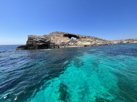 A stunning view of a rocky coastline with an arch, surrounded by crystal-clear turquoise waters — a perfect destination for boat trips and scenic explorations.