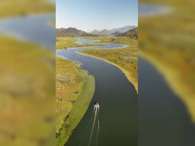 Aerial view of a boat navigating through a winding waterway surrounded by lush greenery and mountains, showcasing the beauty of nature and boating adventures.