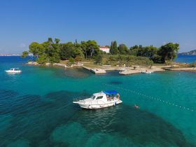 A picturesque scene featuring a boat anchored in clear turquoise waters near an island, with people enjoying the sun and swimming — a perfect getaway for relaxation and adventure.