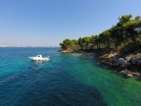 A scenic view of a boat anchored near a lush coastline, showcasing the beauty of the clear turquoise waters and vibrant greenery — perfect for a relaxing day on the water.
