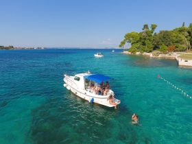A lively group enjoys a day on the water, with some swimming near their boat in stunning turquoise waters — perfect for summer adventures and fun outings.