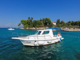 A scenic view of a boat anchored near a picturesque island, with guests enjoying the beautiful coastal surroundings — perfect for a relaxing day on the water.