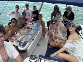 A lively group enjoys a fun day on the water, sharing delicious food and drinks aboard a sailboat — perfect for celebrations and memorable outings.