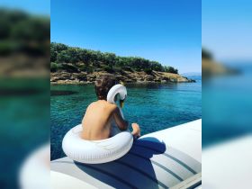A child enjoys a sunny day on the water, sitting in a swan-shaped float, surrounded by serene turquoise waters and lush greenery — a perfect summer moment.