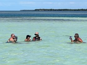 A lively group enjoys drinks while wading in shallow waters, perfect for a fun sandbar stop on a sunny day.