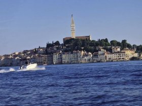 A speedboat glides through the shimmering waters near a picturesque coastline, showcasing the charming architecture of the town in the background — a perfect scene for boating enthusiasts and coastal explorers.