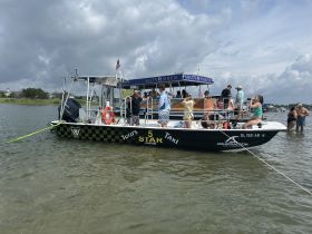 A lively group enjoys a day on the water aboard a boat taxi, with guests swimming and socializing in the shallow waters — perfect for fun-filled outings.