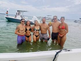 A lively group enjoys a day on the water, swimming and celebrating with drinks in hand, surrounded by boats — perfect for summer fun and beach outings.