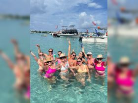 A lively group of friends celebrates in the clear waters, enjoying drinks and fun under the sun — perfect for bachelorette parties or summer getaways.
