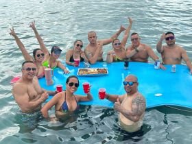 A lively group enjoys a fun day in the water, celebrating with drinks and snacks on a floating table — perfect for summer parties and gatherings.