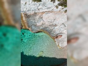 A serene aerial view of a woman relaxing by the crystal-clear waters of a secluded beach, perfect for sunbathing and enjoying nature's beauty.