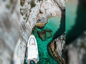 A stunning aerial view of a boat anchored in crystal-clear turquoise waters, surrounded by rocky cliffs — a perfect spot for exploration and relaxation.