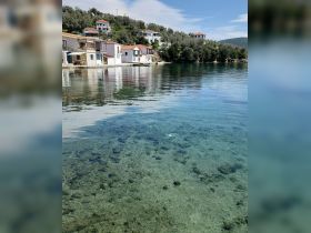 A serene view of a picturesque coastline with clear waters and charming houses, perfect for showcasing beautiful destinations and tranquil harbor settings.