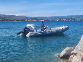 A person navigates a boat in clear blue waters, showcasing a scenic backdrop of the coastline — perfect for exploring the beauty of the sea.