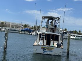 A group of friends enjoys their time aboard the 'Screaming Lines' fishing boat at the marina, ready for an exciting day on the water.
