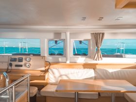 Interior view of a yacht's helm and seating area, showcasing a spacious and well-lit cabin with panoramic windows offering stunning ocean views.