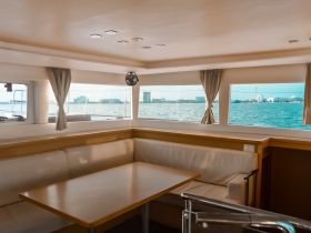 A cozy interior view of a boat's cabin featuring comfortable seating and large windows showcasing a scenic waterfront view.