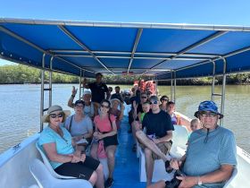 A lively group enjoys a boat tour, smiling and waving as they navigate through scenic waters — perfect for family outings and group adventures.