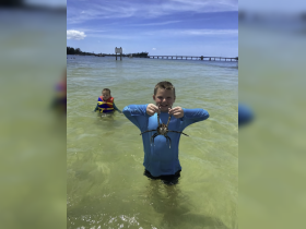Two children enjoy a fun day in the water, with one proudly holding a crab — a delightful moment of wildlife interaction during their aquatic adventure.