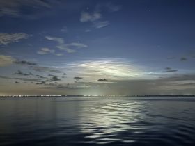 A serene night view over calm waters, showcasing a beautiful sky filled with clouds and distant lights reflecting on the surface — perfect for capturing the tranquility of evening boat trips.