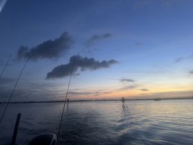 A serene sunset view over the water, with fishing rods visible, capturing the tranquility of an evening fishing trip.