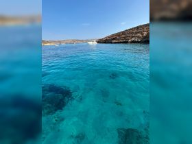 A stunning view of a yacht cruising through crystal-clear turquoise waters, framed by rocky shores — perfect for showcasing the beauty of boating adventures.
