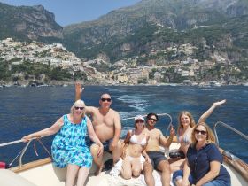A cheerful group enjoys a sunny day on a boat near the stunning coastline of Positano, capturing the essence of a perfect summer getaway.