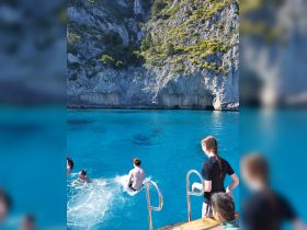 A group of friends enjoys a refreshing swim in crystal-clear waters, with one jumping off the boat — a perfect moment of fun and adventure on the water.