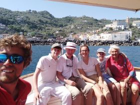 A joyful family poses together on a boat, enjoying a scenic day out on the water, surrounded by beautiful coastal views.