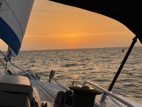 A serene sunset view from the deck of a sailboat, showcasing the tranquil waters and vibrant colors of the evening sky.