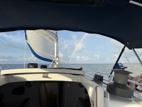 A beautiful view from aboard a sailboat featuring a rainbow in the sky, capturing the essence of a serene sailing experience on the open ocean.