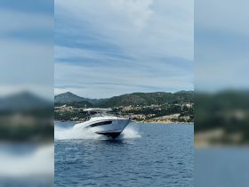 A sleek speedboat glides through the water, showcasing its dynamic design against a scenic backdrop of hills and coastline.