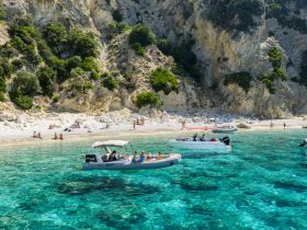 A vibrant scene of people enjoying a sunny day at the beach, with boats anchored in the crystal-clear waters — perfect for a fun day of swimming and relaxation.