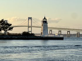 A picturesque view of a lighthouse with a bridge in the background, capturing the serene beauty of the waterfront — perfect for scenic boat tours and photography.