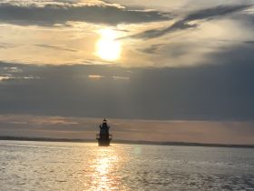 A stunning sunset view featuring a lighthouse silhouetted against the vibrant sky, creating a picturesque scene perfect for evening boat trips.