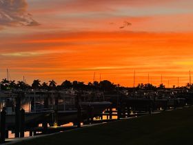 A stunning sunset casts vibrant colors over a marina, showcasing boats docked peacefully in the harbor — a perfect backdrop for evening strolls or romantic getaways.
