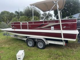 A red Hurricane pontoon boat parked on a trailer, showcasing its sleek design and ready for a day on the water.