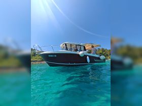 A scenic view of a Merry Fisher boat on crystal-clear waters, with a person enjoying the sun on deck — perfect for summer adventures and coastal exploration.