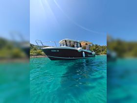 A sleek boat is anchored in crystal-clear waters, showcasing its elegant design against a backdrop of lush greenery — perfect for summer adventures.