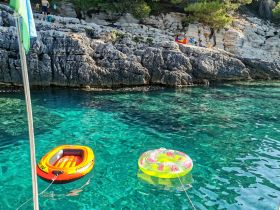 Colorful inflatables float in crystal-clear waters near rocky shores, perfect for a day of relaxation and fun in the sun.