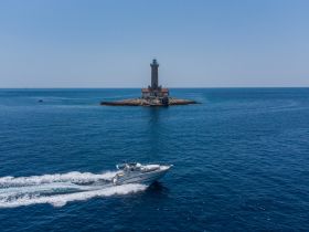 An aerial view captures a boat cruising past a picturesque lighthouse, showcasing the beauty of maritime adventures and coastal scenery.