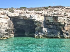 A stunning view of a rocky coastline with a cave entrance, where a person is enjoying the clear turquoise waters — a perfect spot for swimming and exploration.