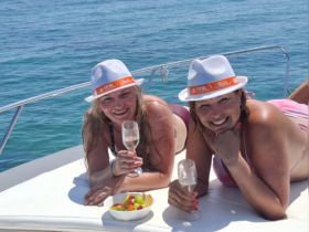 Two friends enjoy a sunny day on a boat, celebrating with cocktails and fresh fruit — a perfect moment for relaxation and fun on the water.