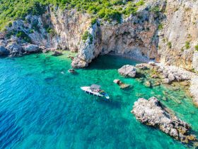 A picturesque view of a boat anchored near a secluded beach, with clear turquoise waters and rocky cliffs, perfect for a day of exploration and relaxation.
