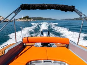 A sleek speedboat cruising through clear blue waters, showcasing its vibrant orange seating and scenic island backdrop — perfect for thrilling adventures on the water.
