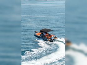 A sleek speedboat navigates through clear waters, showcasing its vibrant orange and gray design while underway.