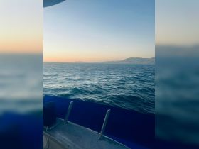A serene view of the ocean from the deck of a boat, showcasing the tranquil waters and distant coastline at sunset.