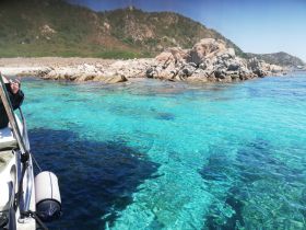 A stunning view of crystal-clear waters and rocky coastline, with a person enjoying the boat ride — perfect for capturing the beauty of a day on the water.