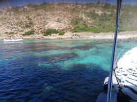 A picturesque view of a group enjoying a sunny day at the beach, with a small boat nearby and crystal-clear waters perfect for swimming.