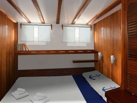 Cozy interior cabin of a boat featuring wooden paneling, a comfortable bed with nautical-themed bedding, and natural light filtering through the windows, perfect for relaxing during a voyage.